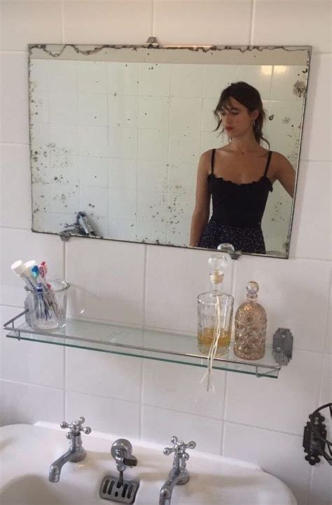 A Woman Standing In Front Of A Bathroom Mirror Next To A Sink And Faucet