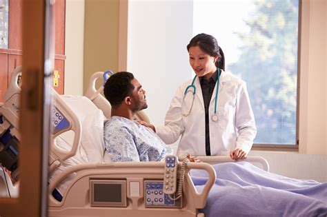 Female Doctor Talking To Male Patient In Hospital Bed Stock Photo