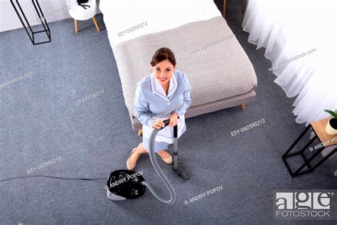 Happy Young Housekeeper Cleaning Carpet With Vacuum Cleaner In Hotel