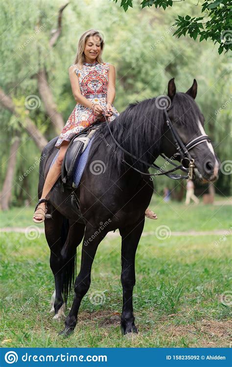 Young Woman In A Bright Colorful Dress Riding A Black Horse Stock Photo