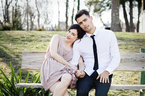 Portrait Of Happy Couple Sitting On Bench At Park Stock Photo