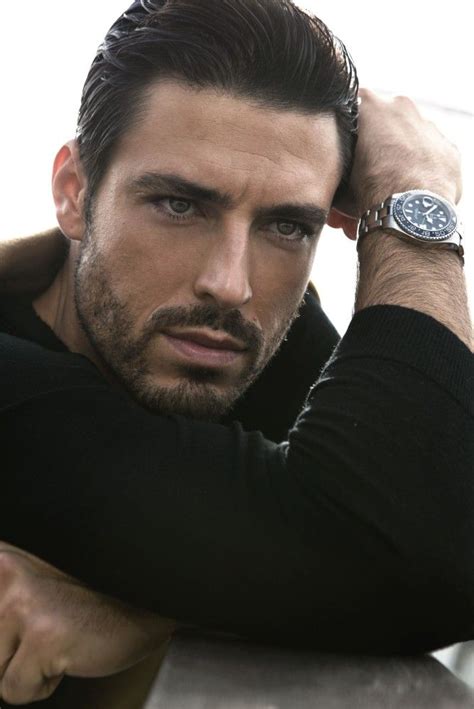 A Man With A Watch On His Wrist Leaning Against A Wall And Looking At The Camera