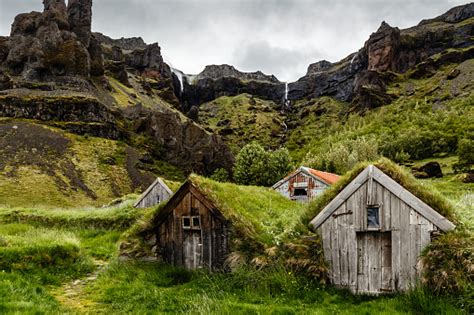 Icelandic Turf Houses And Rocks With Waterfall In The Background Near