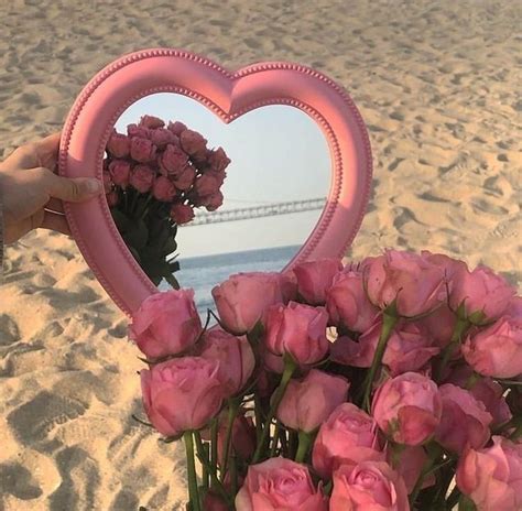 Someone Holding Up A Heart Shaped Mirror With Pink Roses In Front Of It