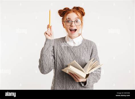 Portrait Of An Excited Young School Nerd Girl Holding Book And Pointing Up Isolated Over White