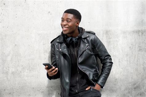 Young Black Man In Leather Jacket Smiling While Holding Cellphone Stock