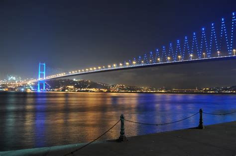 The Blue Bridge Is Lit Up At Night Over The Water With Lights