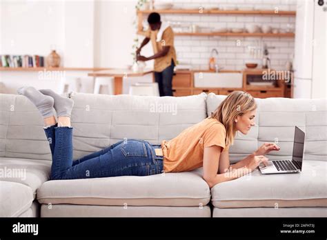 Woman Relaxing Lying On Sofa At Home Using Laptop Computer With Man In