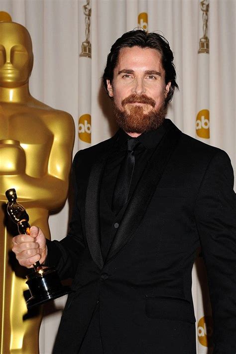 A Bearded Man In A Tuxedo Holding An Oscar For Best Performance By An Actor