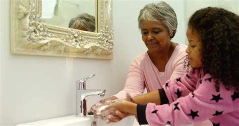 Grandmother Teaching Granddaughter To Wash Her Hands In Bathroom At