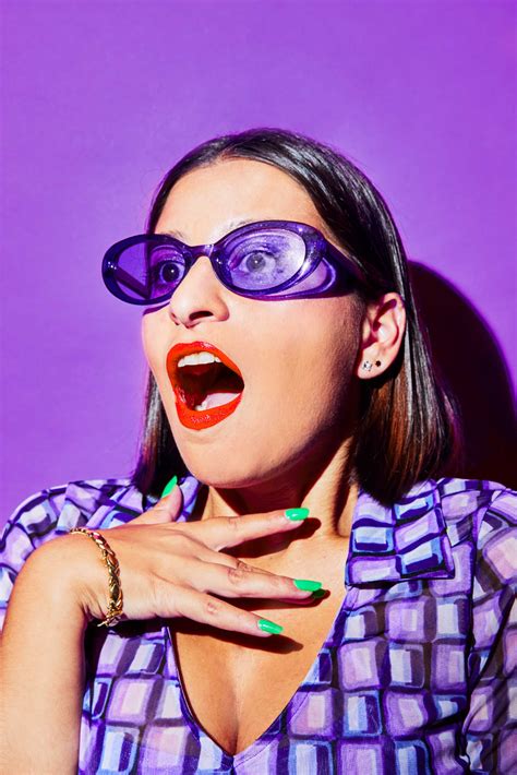 A Woman With Purple Glasses On Her Face And Green Nail Polish In Front Of A Purple Background