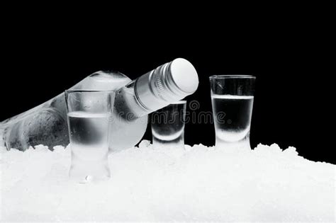 Bottle With Glasses Of Vodka Lying On Ice On Black Background Stock