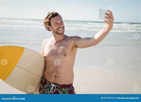 Smiling Shirtless Man Taking Selfie With Surfboard At Beach Stock Image