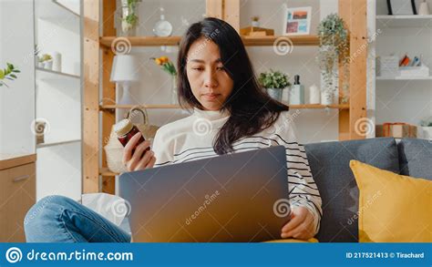 Sick Young Asian Woman Hold Medicine Sit On Couch Video Call With Laptop Consult With Doctor At