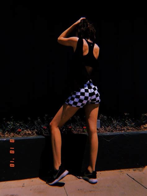 A Woman In Black And White Checkered Shorts Leaning Against A Wall With