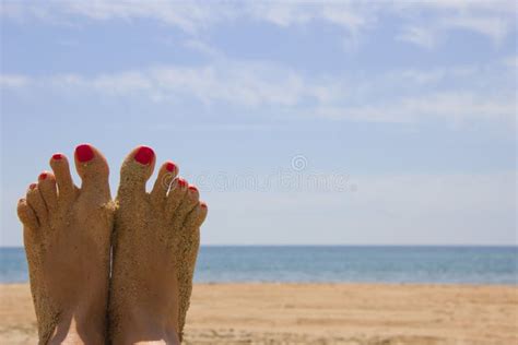 Female Tanned Legs With A Bright Pedicure On The Sandy Beach Stock
