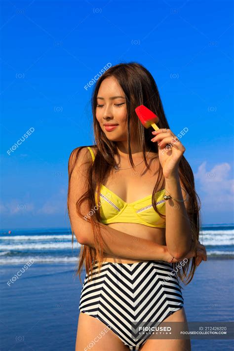 asian girl on a beach in bikini with an ice cream in her hand — women