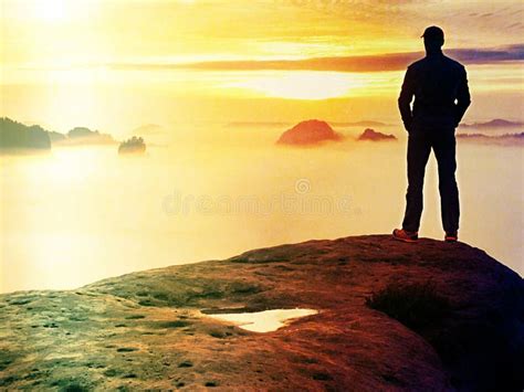 Man Stands Alone On The Peak Of Rock Hiker Watching To Autumn Sun At