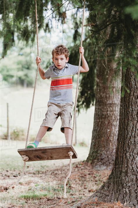 You left me wondering why all these thoughts i keep in my head the words you spoke were so kind so why am i feeling so sad? Vertical front view of boy standing on swing under pine ...