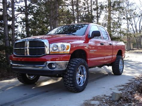 A Red Dodge Ram Truck Parked On The Side Of A Road In Front Of Some Trees