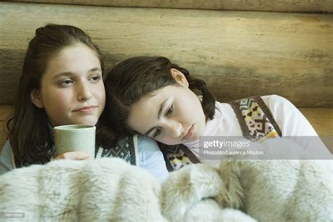 Two Teen Girls In Winter Clothes Sitting Under Warm Blanket Together