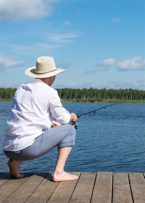 A Fisherman Is Sitting On A Pier With A Fishing Rod Waiting For A Big
