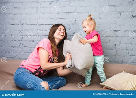 Mom And Daughter Play On The Couch With Pillows Fight Dressed In Bright Stylish Clothes In A