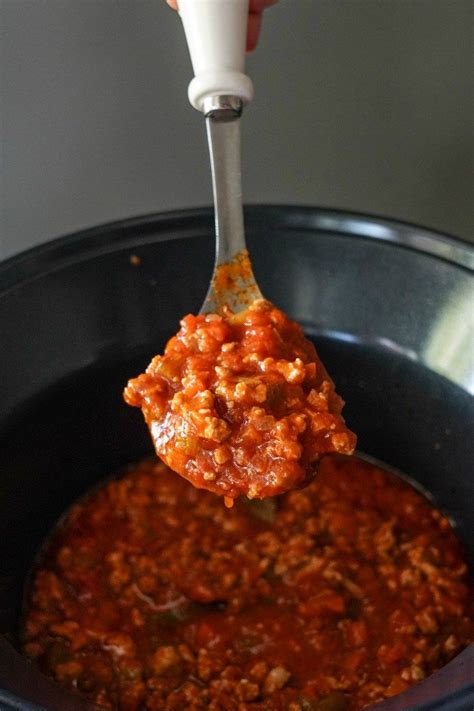 A Spoon Full Of Chili Sauce Being Lifted From A Crock Pot