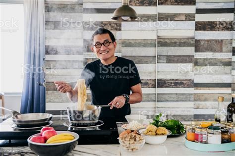 Cheerful Chinese Man Cooking Pasta In Domestic Kitchen Stock Photo