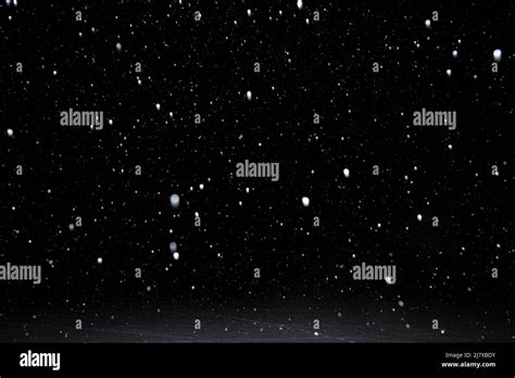 Real Falling White Snow Against Black Night Sky Above Snowy Ground In