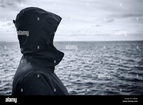 Faceless Hooded Person Looking Into Distance At Horizon Over The Sea