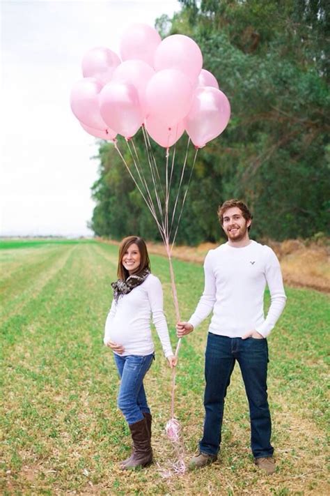 A Pregnant Couple Holding Pink Balloons In The Grass