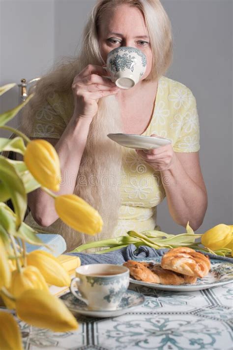 middle aged blonde woman with long hair drinks and eat drinking coffee and tea stock image