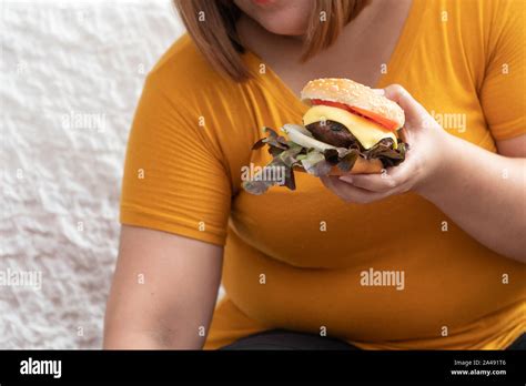 hungry overweight woman smiling and holding hamburger and sitting in the bedroom her very happy