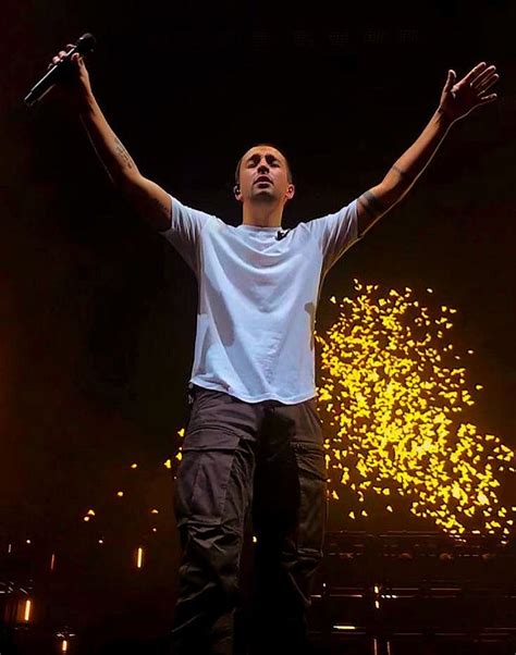 A Man Standing On Top Of A Stage Holding His Hands Up In The Air With
