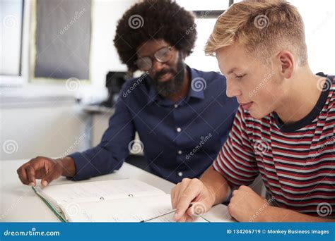 High School Tutor Giving Male Student One To One Tuition At Desk In