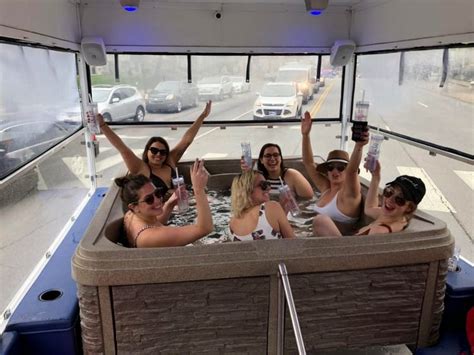 Four Women Sitting In A Hot Tub With Their Hands Up To The Sky And Holding Drinks