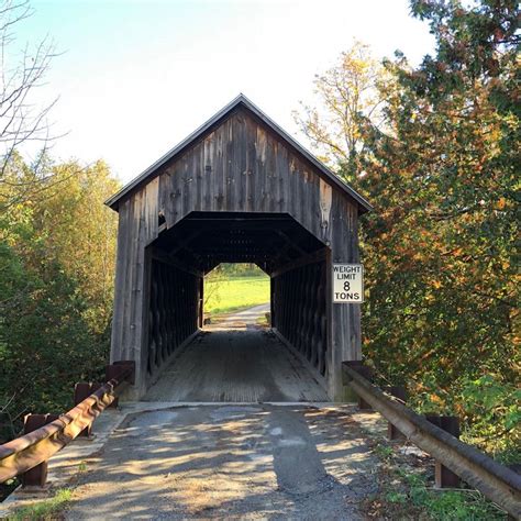A Wooden Covered Bridge Over A Dirt Road In The Middle Of Some Trees