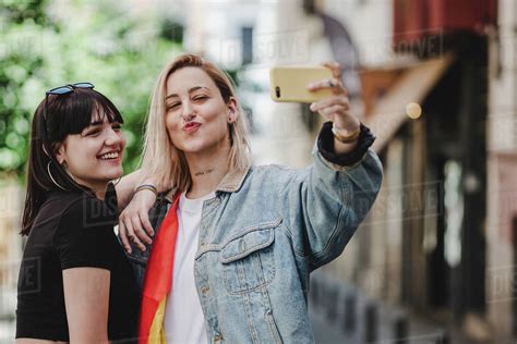 Cheerful Young Lesbians Smiling And Posing For Selfie While Standing On City Street Stock