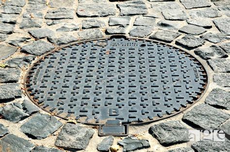 Metal Sewer Hatch Is On The Granite Block Pavement Stock Photo