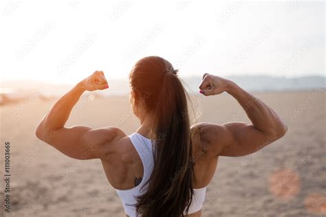 Young Fitness Woman Flexing Big Strong Biceps Muscles Towards The Sun