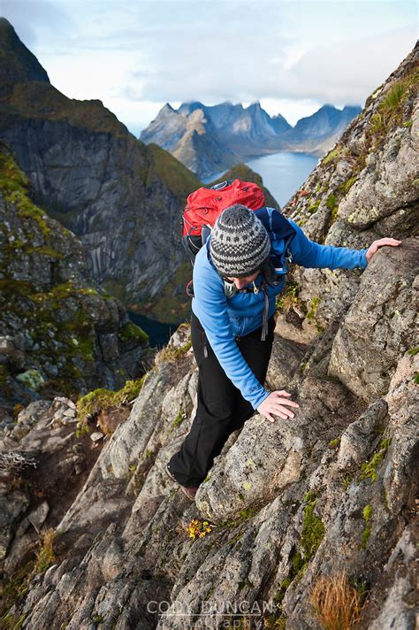 Female Hiker Climbs Rocks Near Summit Of Reinebringen Moskenesoy