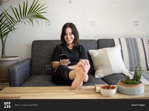 Woman Sitting On Couch With Feet Up On Phone Stock Photo Offset
