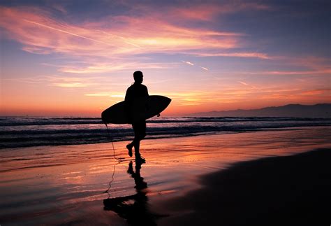 Person Holding Surfboard While Walking In The Beach At Night Time Los