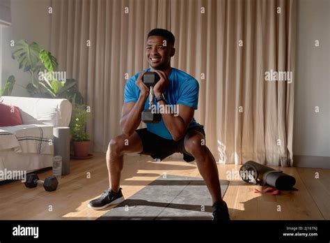 African American Male Squatting In Lounge Holding Dumbbell Weight