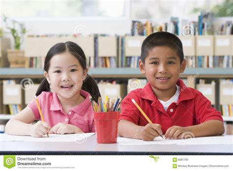 Children Sitting At Desk And Writing In Classroom Stock