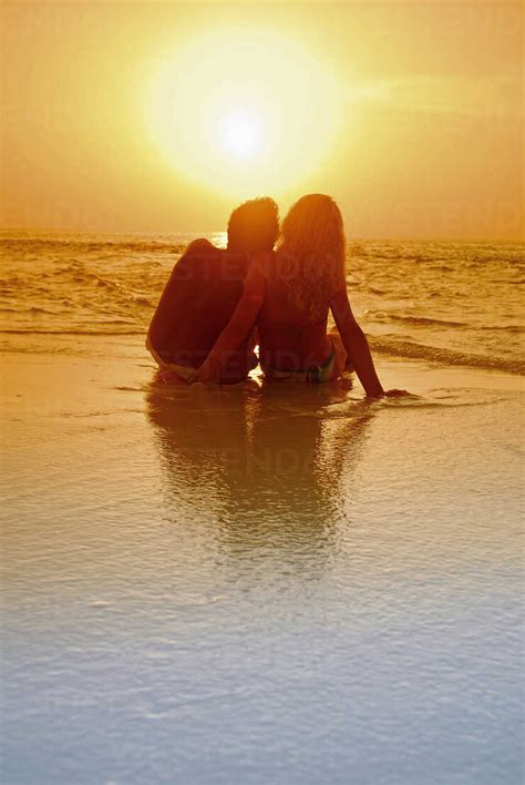 Couple Sitting At The Beach Silhouetted At Sunset Maldives Stock Photo