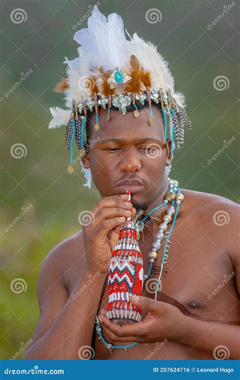 A Traditional African Dressed Male With A Beaded Headdress Drink From A