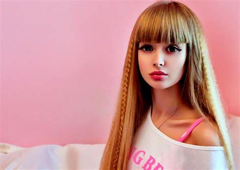 A Barbie Doll With Long Blonde Hair Wearing A Pink T Shirt Against A
