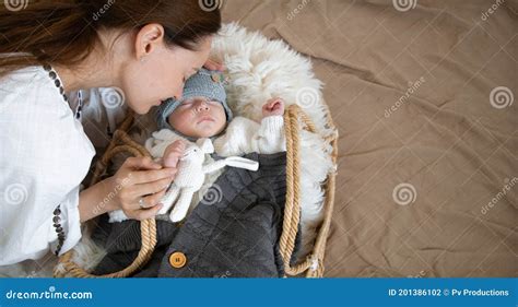 Sleepy Baby In A Wicker Cradle In Warmth Near A Happy Caring Mother